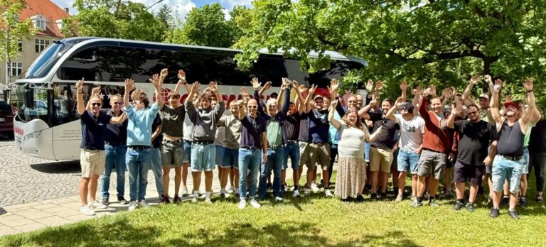 Gruppe winkt vor Reisebus unter grünen Bäumen