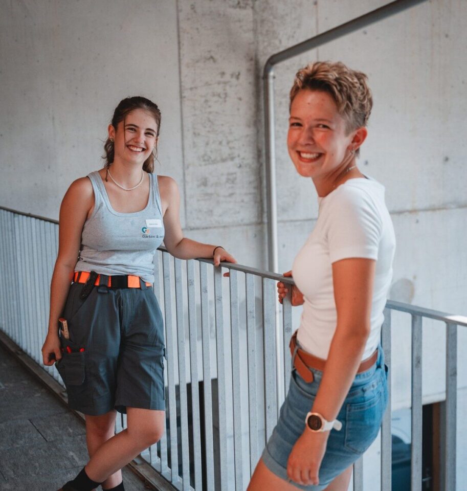 Zwei lächelnde Frauen auf einer Betontreppe mit Geländer