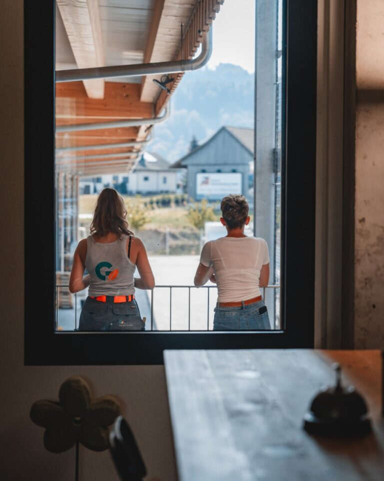 Zwei Frauen stehen auf einem Balkon vor Bergkulisse
