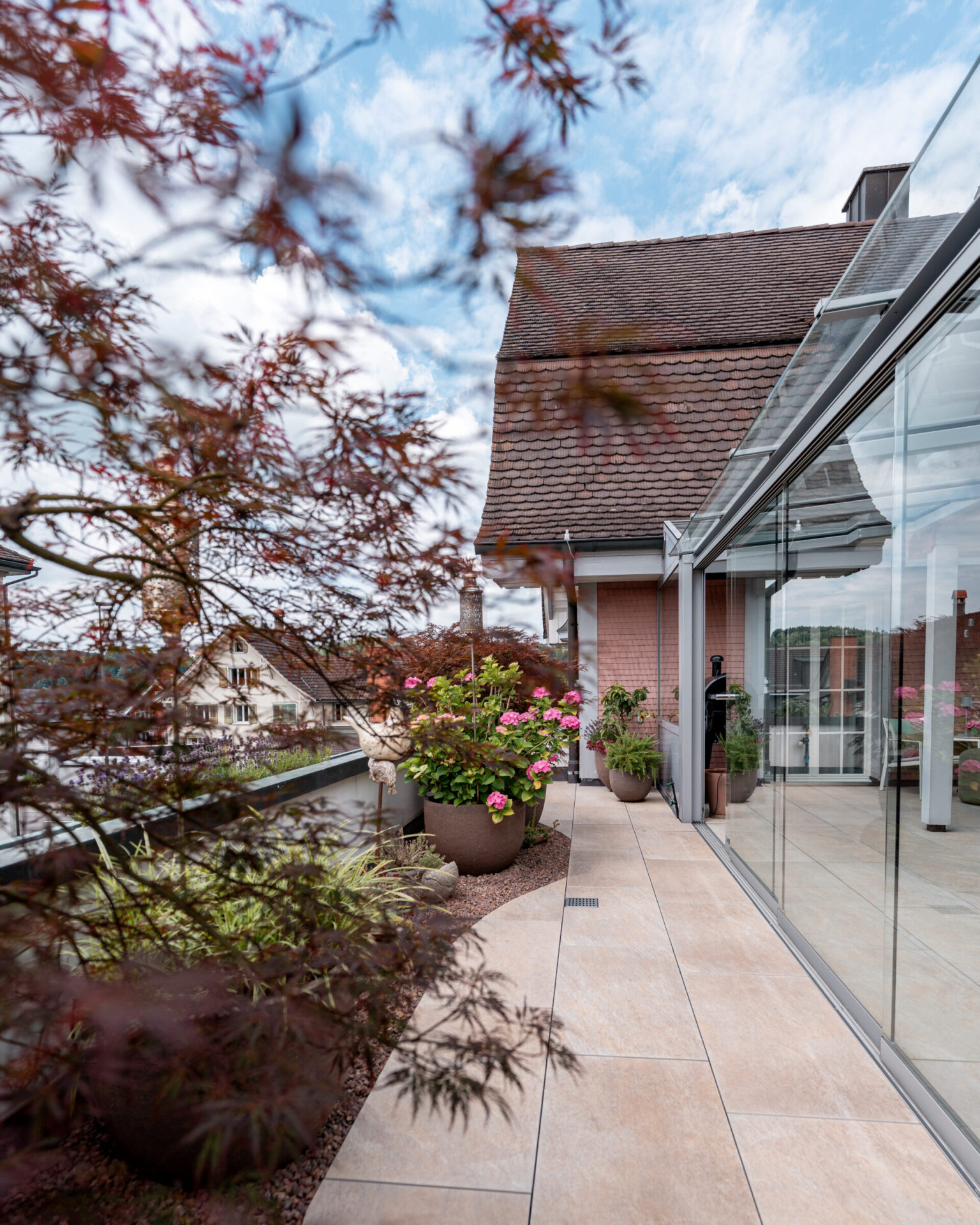 Dachterrasse mit Pflanzen und Glasfassade bei schönem Wetter.