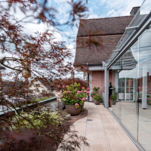 Dachterrasse mit Pflanzen und Glasfassade bei schönem Wetter.
