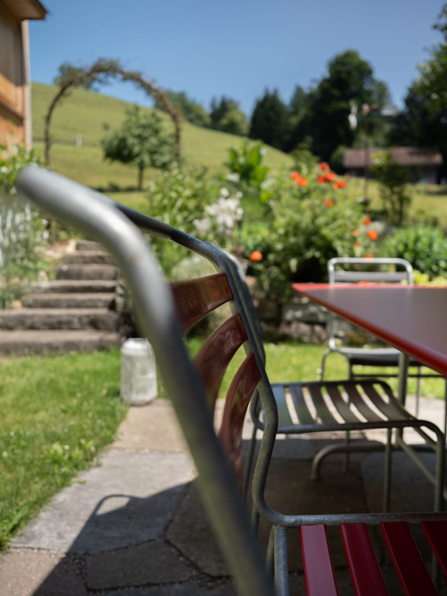 Roter Gartenstuhl vor grünem Garten und Torbogen.