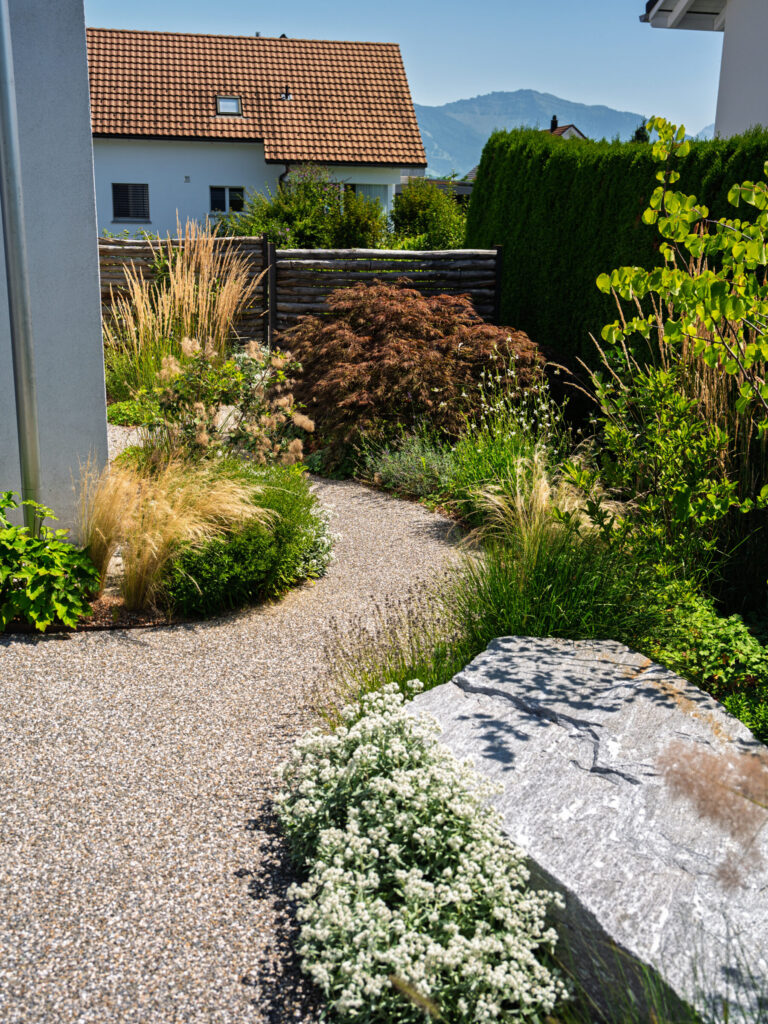 Grüner Gartenweg mit blühenden Pflanzen und Stein.