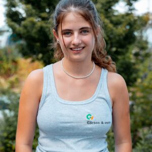 Lächelnde junge Frau im Garten mit Arbeitskleidung