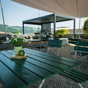 Sonnige Terrasse mit Tischen und Stühlen im Freien.