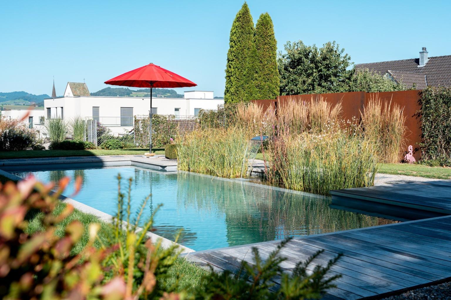 Moderner Pool im Garten mit rotem Sonnenschirm.