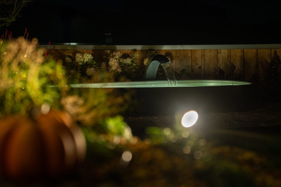 Nachts beleuchteter Gartenbrunnen mit Holzumrandung