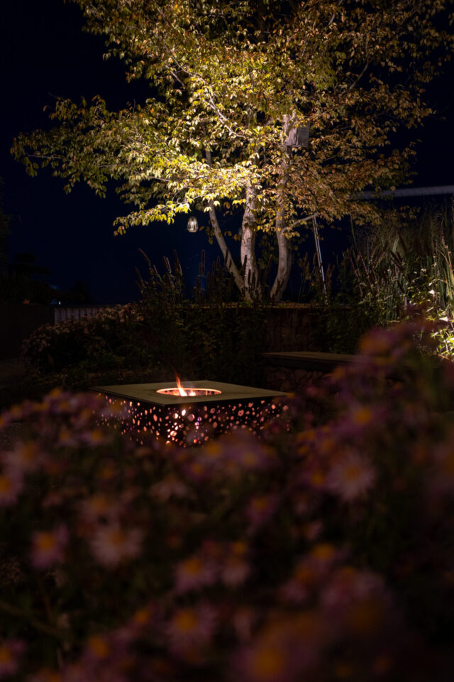 Beleuchteter Garten mit Baum und Feuerstelle bei Nacht