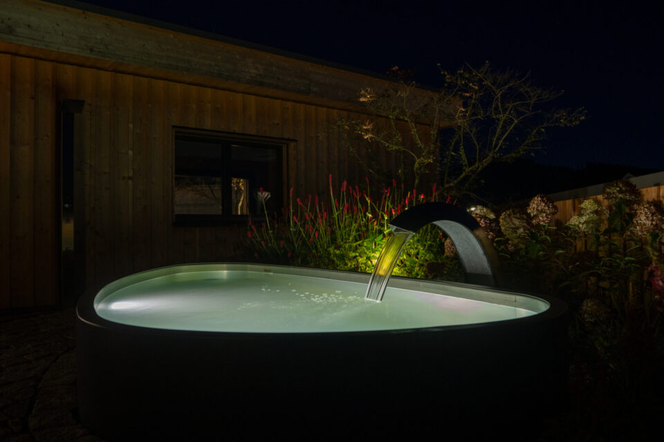 Beleuchteter Whirlpool im Garten bei Nacht.