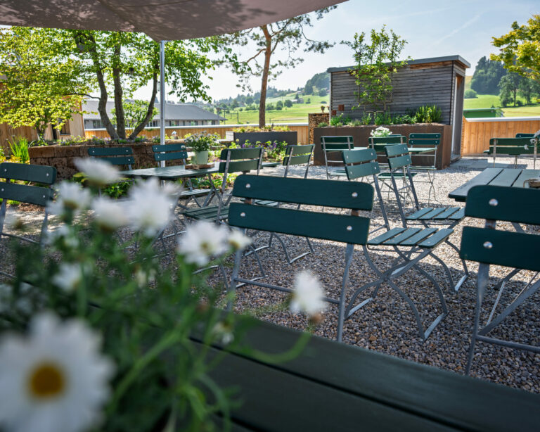 Sonnige Terrasse mit leeren Bistromöbeln und Blumen.