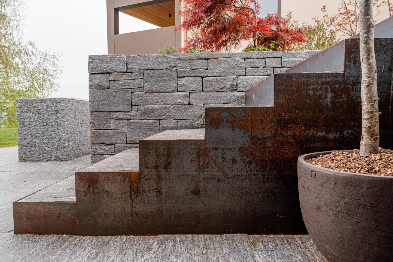 Rostige Metalltreppe an Steinmauer mit Baum im Topf.