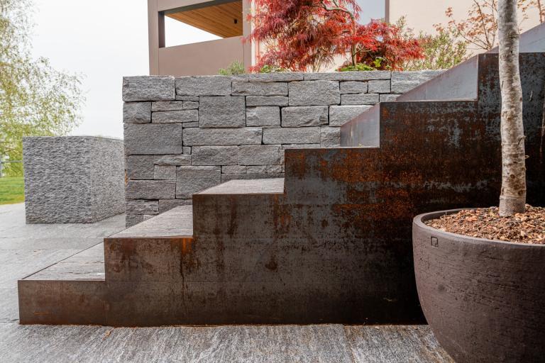 Rostige Metalltreppe an Steinmauer mit Baum im Topf.
