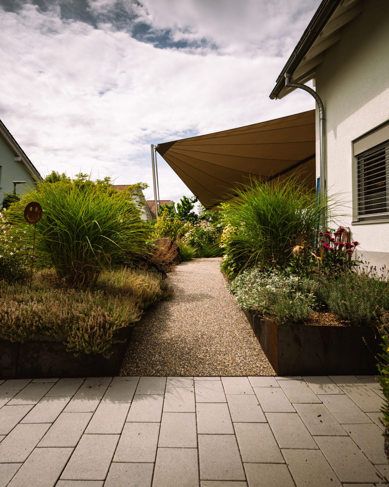 Gartenweg mit Pflanzen und Sonnensegel.