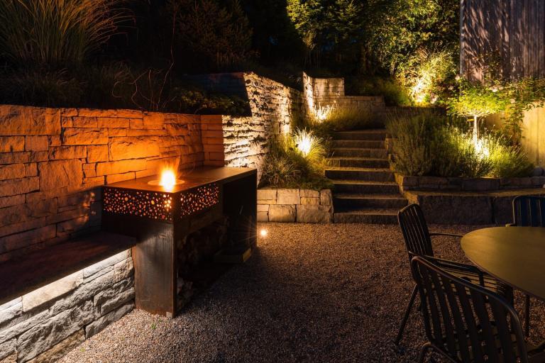 Nachtbeleuchteter Garten mit Feuerstelle und Sitzbereich.