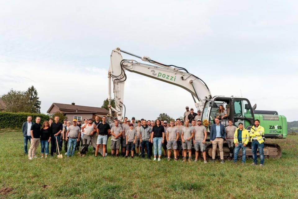 Bauteam vor grünem Bagger auf einer Wiese