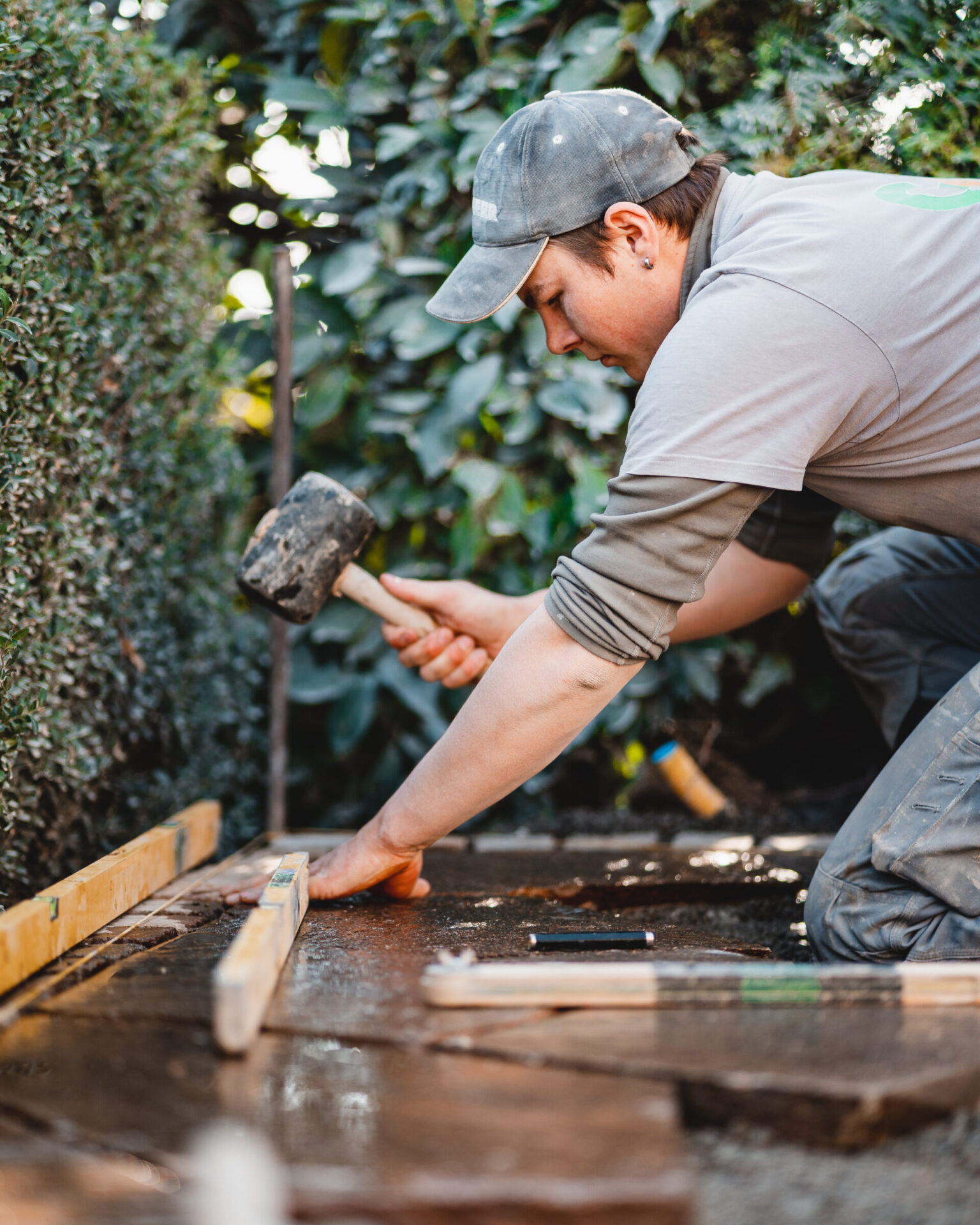 Gartenarbeiter pflastert Terrasse mit Hammer und Holzlatte.